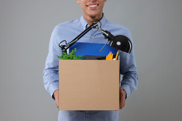 Unemployed young man with box of personal office belongings on grey background, closeup
