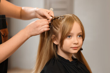 Fototapeta premium Professional hairdresser braiding girl's hair in beauty salon, closeup
