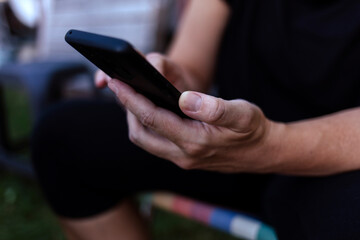 A unrecognized women sits on a chair in nature and holds a smartphone. The concept of communication via the internet.