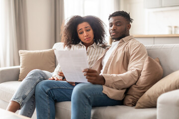Obraz premium Stressed married young black couple looking at loan documents indoor
