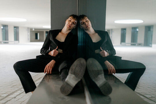 Trans young man with eyes closed sitting on seat by window in basement