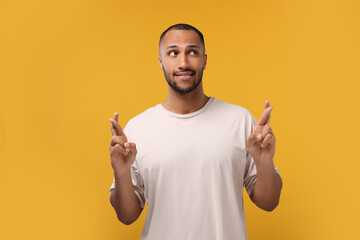 Young man crossing his fingers on orange background
