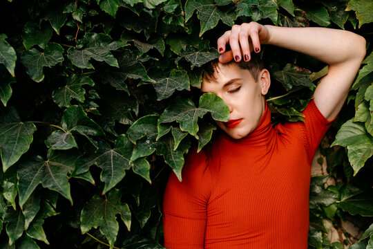 Contemplating gender fluid man standing against leaves in park