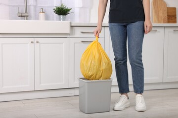 Woman taking garbage bag out of trash bin in kitchen, closeup. Space for text