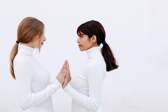 Young women touching hands while looking at each other against white background