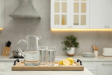Fototapeta na wymiar Jug, glasses with clear water and lemons on white table in kitchen, space for text