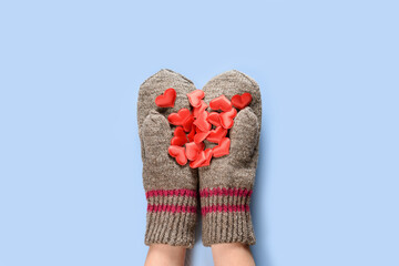 Female hands in mittens hold red hearts on blue background.