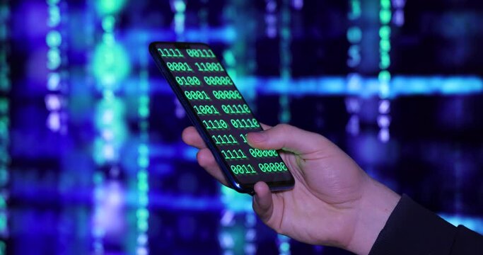 Close up of cell phone in the hand of a young hacker or programmer. On the background screen and phone screen program code and software. Hacking or programming concept
