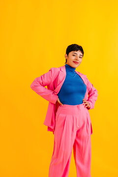 Confident smiling young woman wearing blazer standing against yellow background