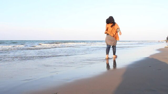 Woman in gamis shirt close up walking on wet sand and ocean waves lightly touching feet enjoying winter trip to tropical resort with deserted beach. Vacation, travel, concept 