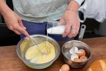 Make an omelet for breakfast. Hands pour milk from a glass into eggs.