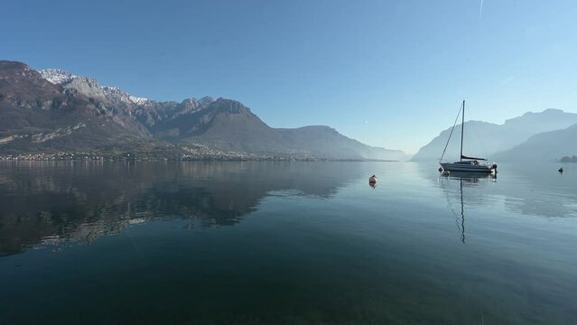 A general view of the tranquil waters and surrounding mountains in Oliveto Lario, Lake of Como, Lombardy, Italy. A small sailing boat lays moored. Early morning light. 