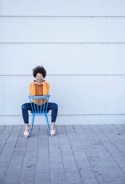 Smiling young woman sitting on chair in front of wall