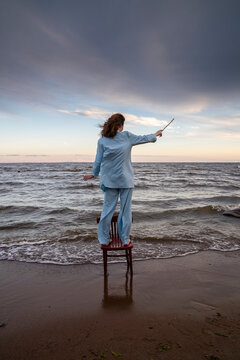 Young woman standing on chair and gesturing with stick in front of sea