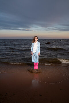 Woman wearing pink rubber boots standing on rock at sunset