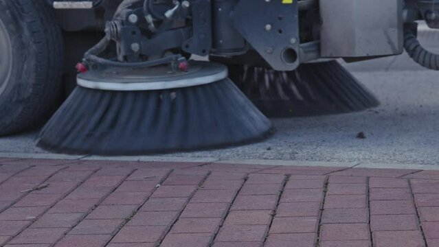 Street sweeper truck with rotating brushes cleaning the sidewalk pavement surface, slow motion