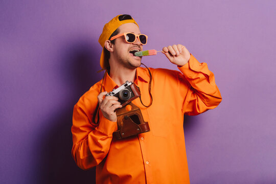 Stylish man in orange shirt with camera and ice cream against purple background