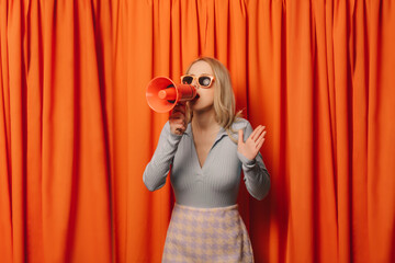 Woman making announcement through megaphone in front of orange curtain