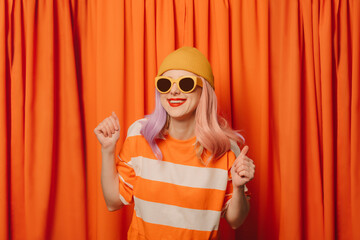 Happy woman with clenched fists dancing in front of orange curtain