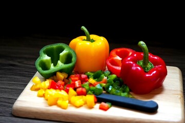 Multi color fresh sweet bell pepper sliced with knife on wooden cutting board in the kitchen room