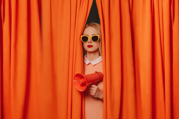 Woman wearing sunglasses standing with megaphone amidst curtains