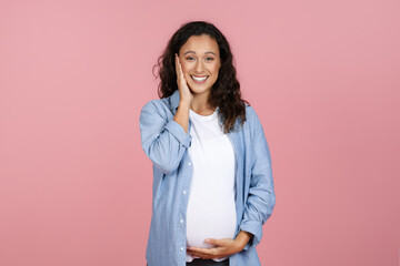 Happy pregnant woman touching her face and belly
