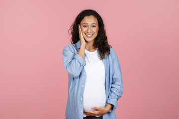Fototapeta premium Happy pregnant woman touching her face and belly