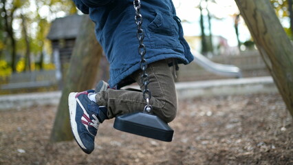 One small boy on top of park swing during autumn fall season. 3 year old child engaged in outdoor play