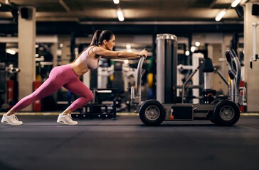 A strong sportswoman is pushing machine for strengthening gluteus and legs.