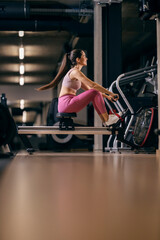 Obraz na płótnie Canvas A sportswoman is exercising on rowing machine in a gym.
