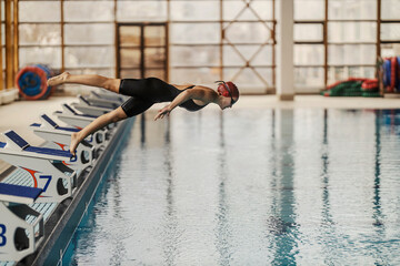A young female swimmer is diving and jumping into the swimming pool on her training. - Powered by Adobe