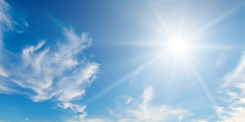 There are light white clouds and bright sun in the blue sky. Wide photo.