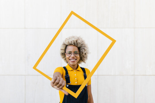 Woman holding yellow frame in front of wall