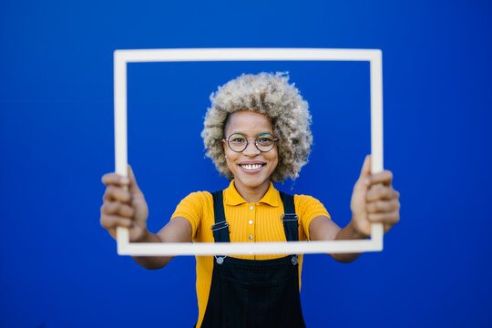 Smiling woman holding frame in front of blue wall