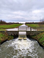 Fototapeta na wymiar A floodgate between two canals with a small artificial waterfall and a wooden railing. Dutch landscape. 