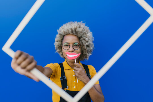 Woman holding frame and smile prop in front of wall