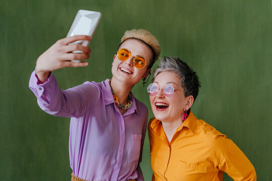 Happy young woman taking selfie with mother in front of green wall