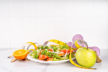 Weight loss, Healthy lifestyle, diet food, sport and fitness concept. Fresh balanced vegetable and chicken breast salad with fruit, fitness equipment, dumbbell, measuring tape on a white background