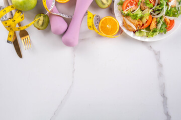 Weight loss, Healthy lifestyle, diet food, sport and fitness concept. Fresh balanced vegetable and chicken breast salad with fruit, fitness equipment, dumbbell, measuring tape on a white background