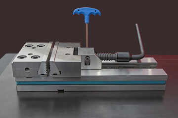 Precision modular vise on metal table black background. Mixed red and white lighting.