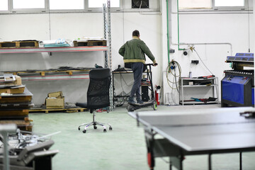 engineer in an electronic repair shop workshop rides electric scooter in a factory