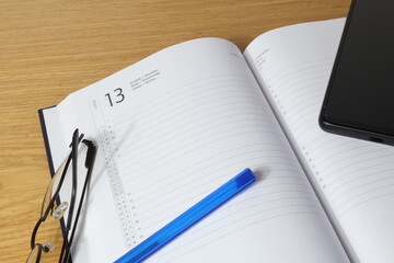 Open diary page italien with biro pen and glasses and cell phone.