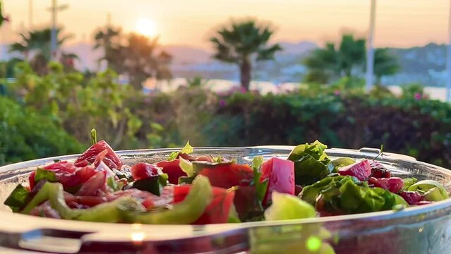 Bowl of fresh garden salad with ripe tomatoes, crisp greens, and peppers, served at sunset by the sea