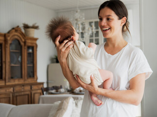 Loving mom carying of her newborn baby at home. Woman holding a baby at the kitchenroom.