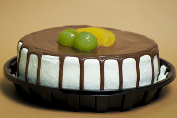 A cream cake topped with milk chocolate and decorated with two white grapes and peach slices in a...