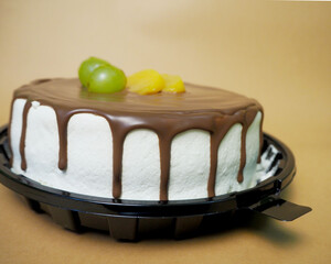 cream cake topped with milk chocolate and decorated with two white grapes and peach slices stands...