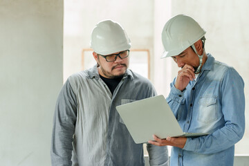 Architects, designers and engineers staff Manager foreman Asian male Standing holding laptop consulting looking stressed about structure house wearing white safety helmet prevent things from falling.