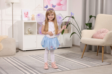 Cute little girl in fairy costume with violet wings and magic wand at home