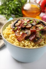 Tasty millet porridge with mushrooms, bacon and green onion in bowl on white table, closeup