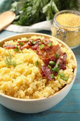 Tasty millet porridge with bacon, green onion and dill in bowl on light blue wooden table, closeup